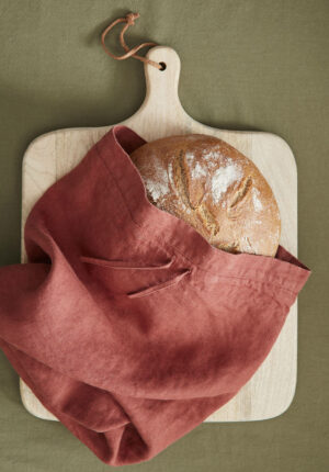 roter Brotbeutel aus Leinen auf Holzbrett mit Brot