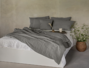 Bett mit grauer Leinen Bettwäsche und Blumentopf rechts daneben